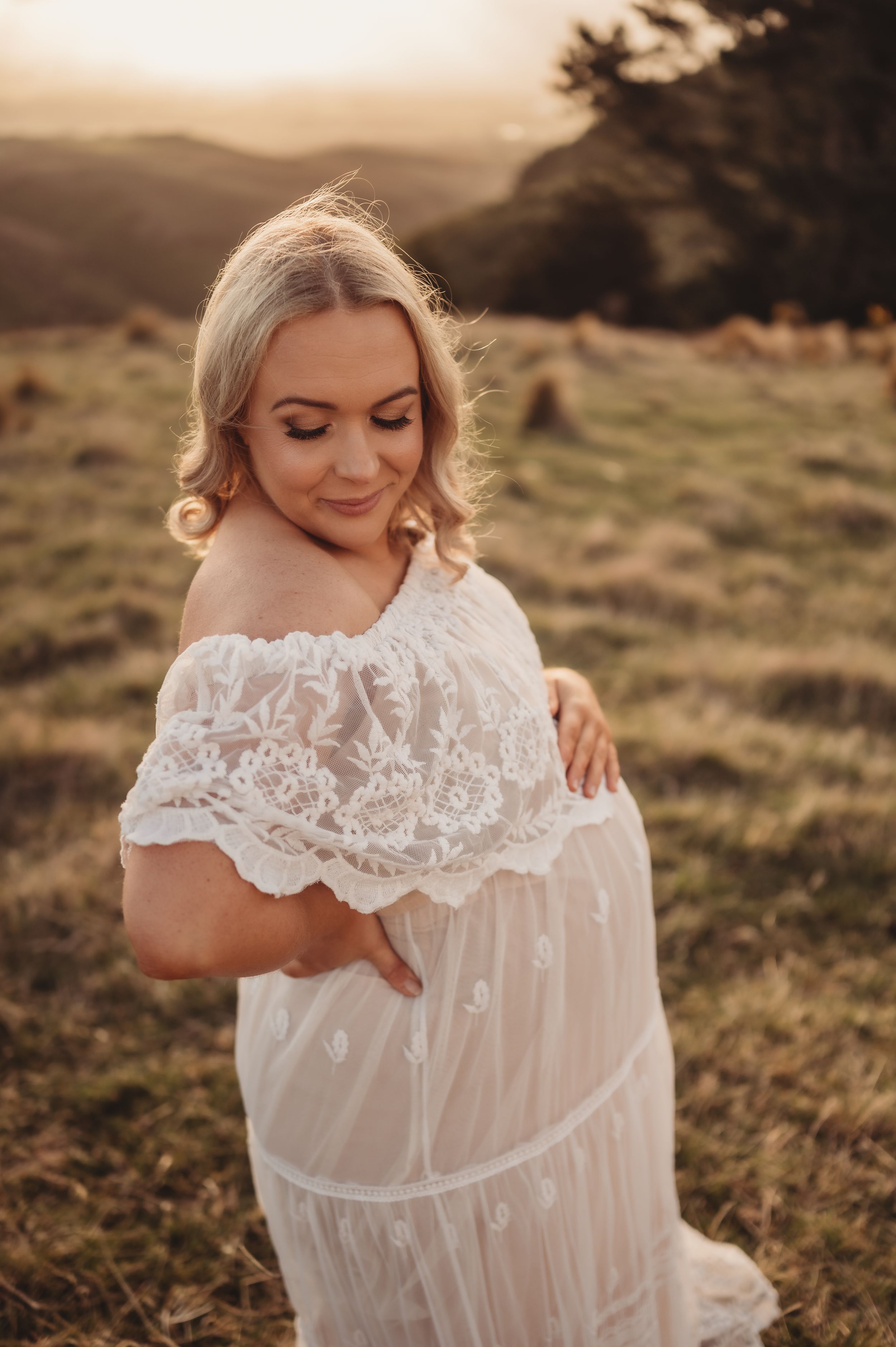 Dreamy outdoor maternity photo featuring delicate white lace dress in mountain setting.
