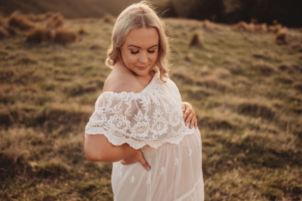 Mother-to-be in white lace dress touching belly during sunset maternity shoot.