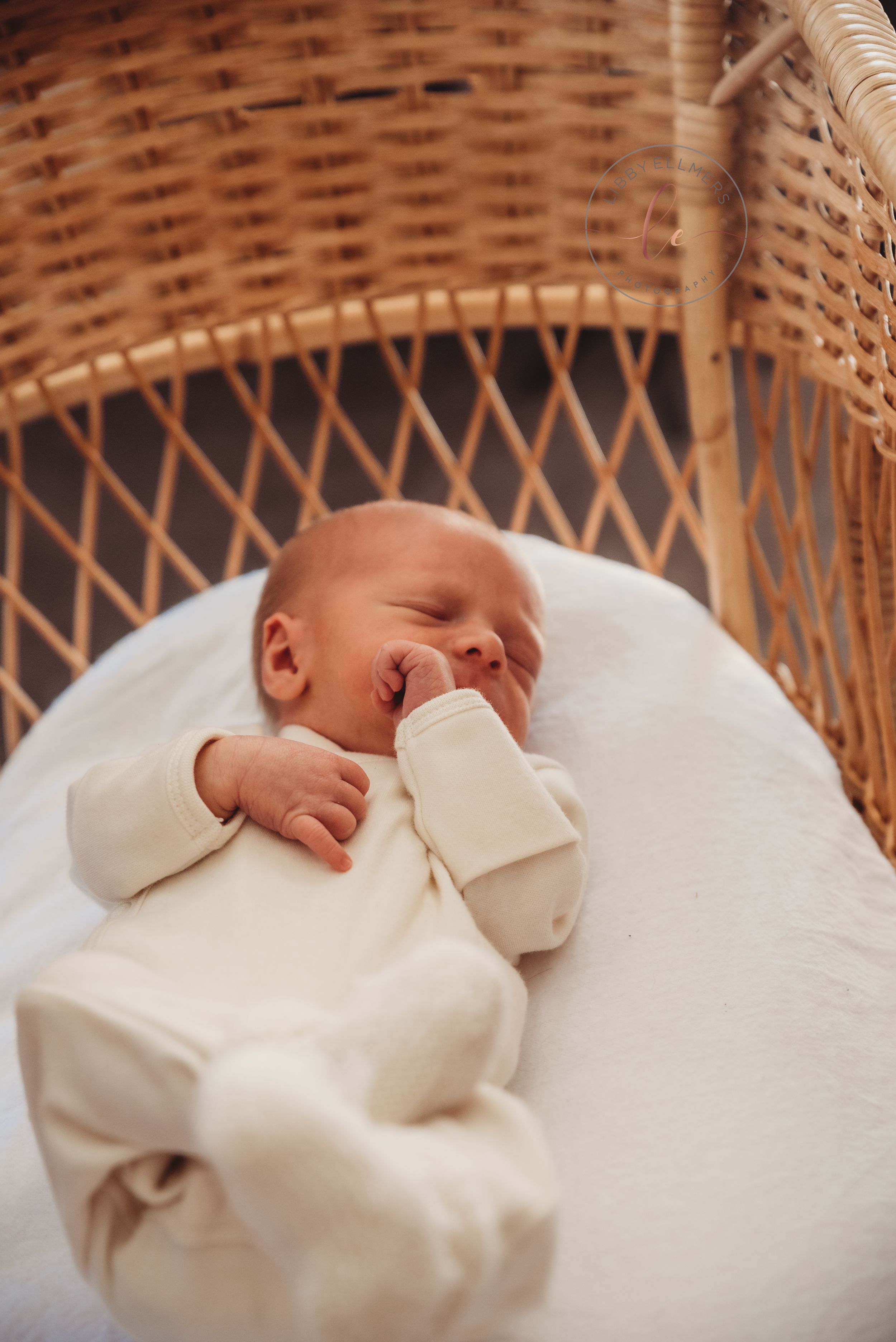 Sleeping baby in cream colored outfit resting in wicker bassinet.