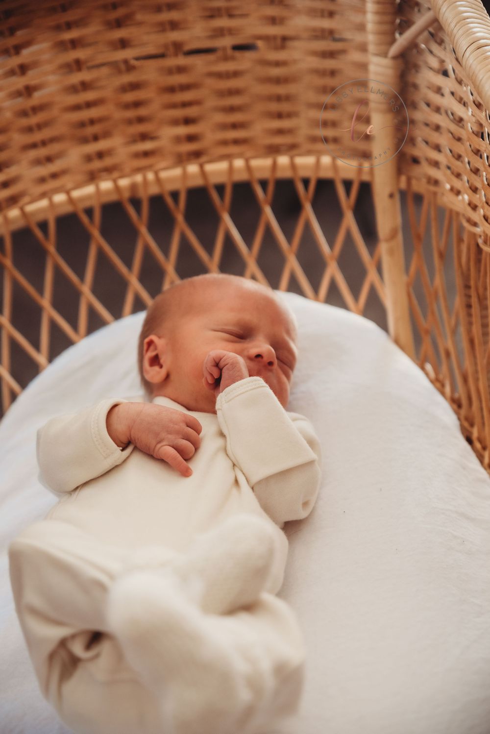 Sleeping baby in cream colored outfit resting in wicker bassinet.