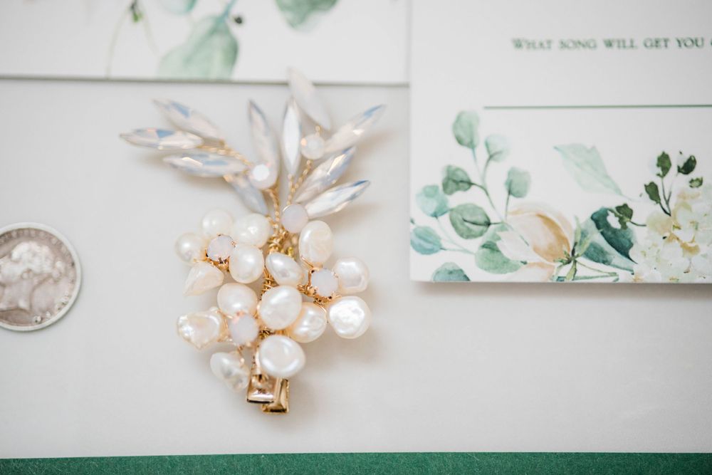 Pearl and gold floral brooch next to watercolor wedding stationery.