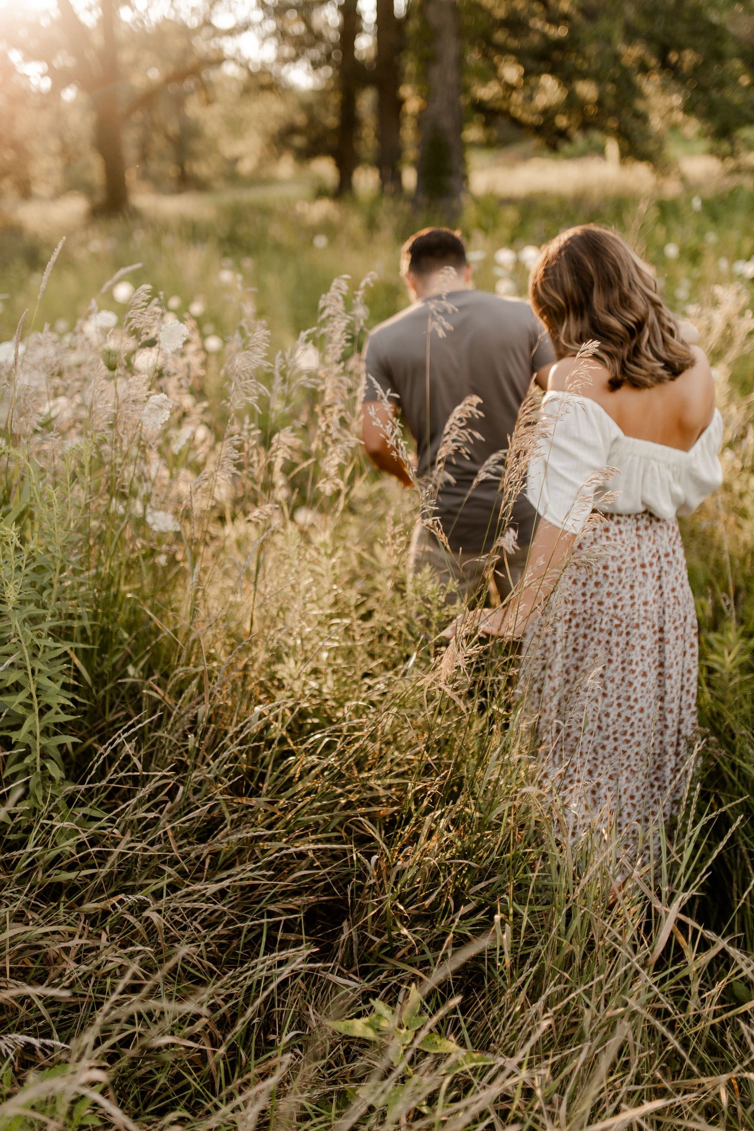 Romantic couple walking through tall grass in summer field at sunset.