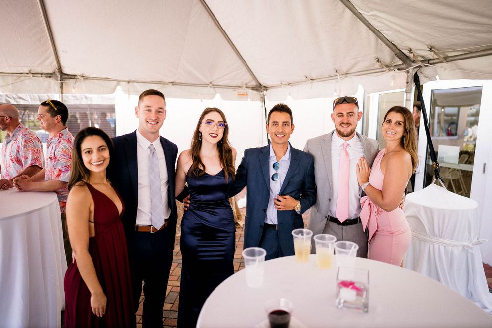 A group of wedding guests pose together under a white tent at an elegant reception.