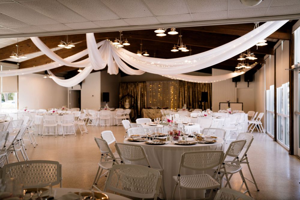 Wedding reception venue decorated with white draping and round tables with folding chairs.