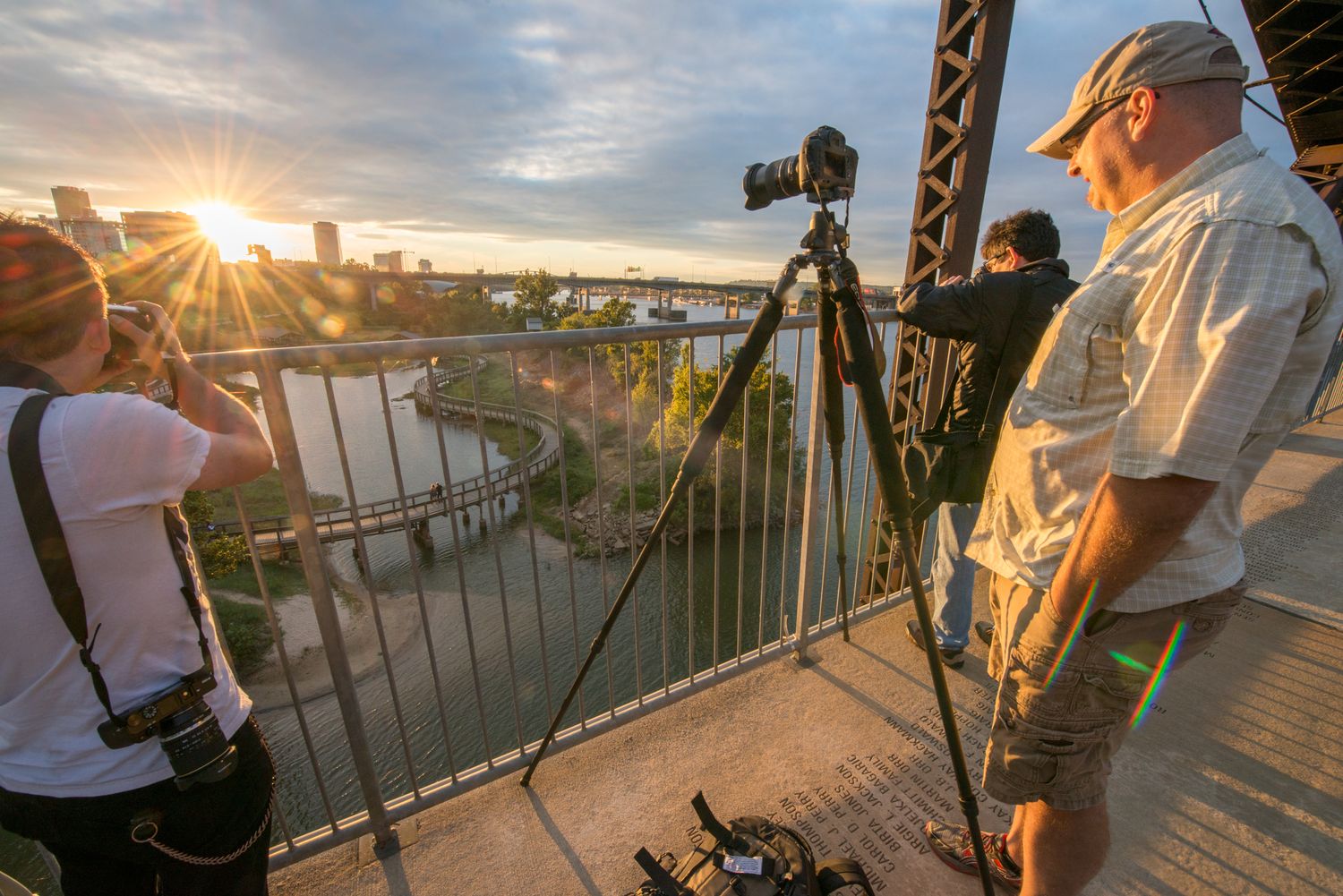 3 photographers on a bridge photographing the Little Rock skyline facing toward the setting starburst sun