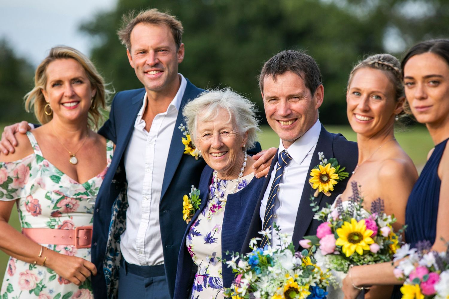 Wedding party poses outdoors with bright sunflowers and colorful floral attire.