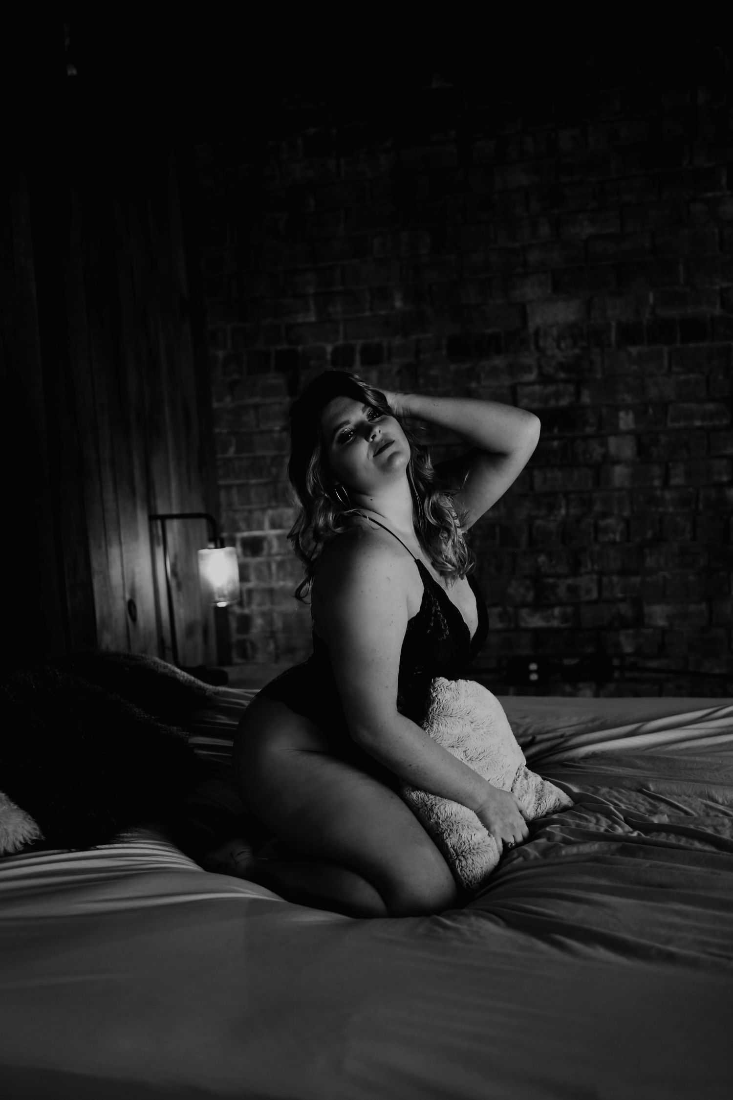 Moody boudoir photography with dramatic shadows against exposed brick wall.