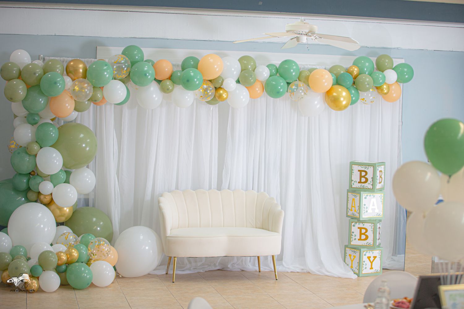 Baby shower backdrop with green and white balloon arch and decorative blocks.
