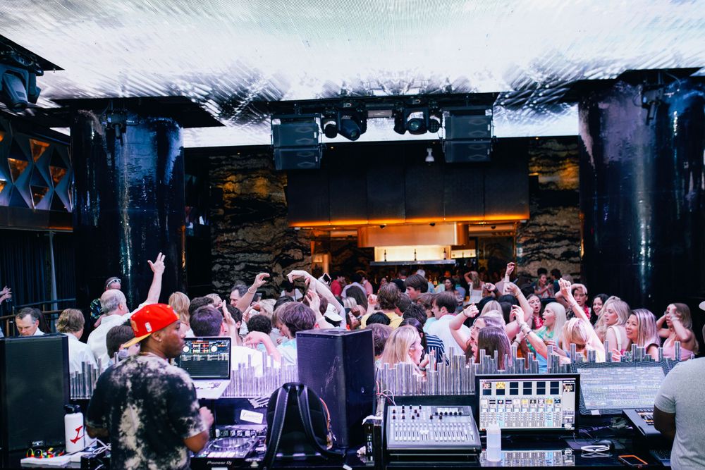 Crowded nightclub scene with DJ booth and dancing crowd.