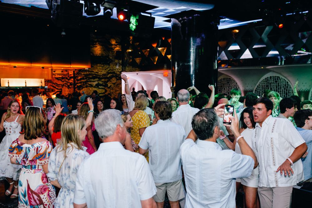 Energetic crowd of party-goers dancing and celebrating in white attire.