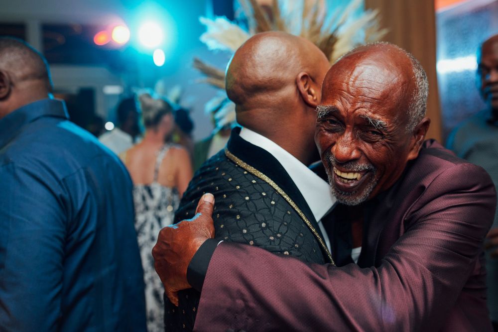 Two men share a warm embrace at an evening celebration with blue lighting.