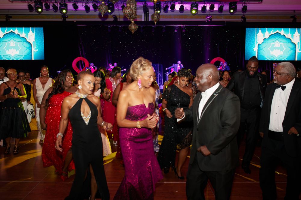 Guests dancing and celebrating at an elegant formal event with purple lighting and decorative displays.