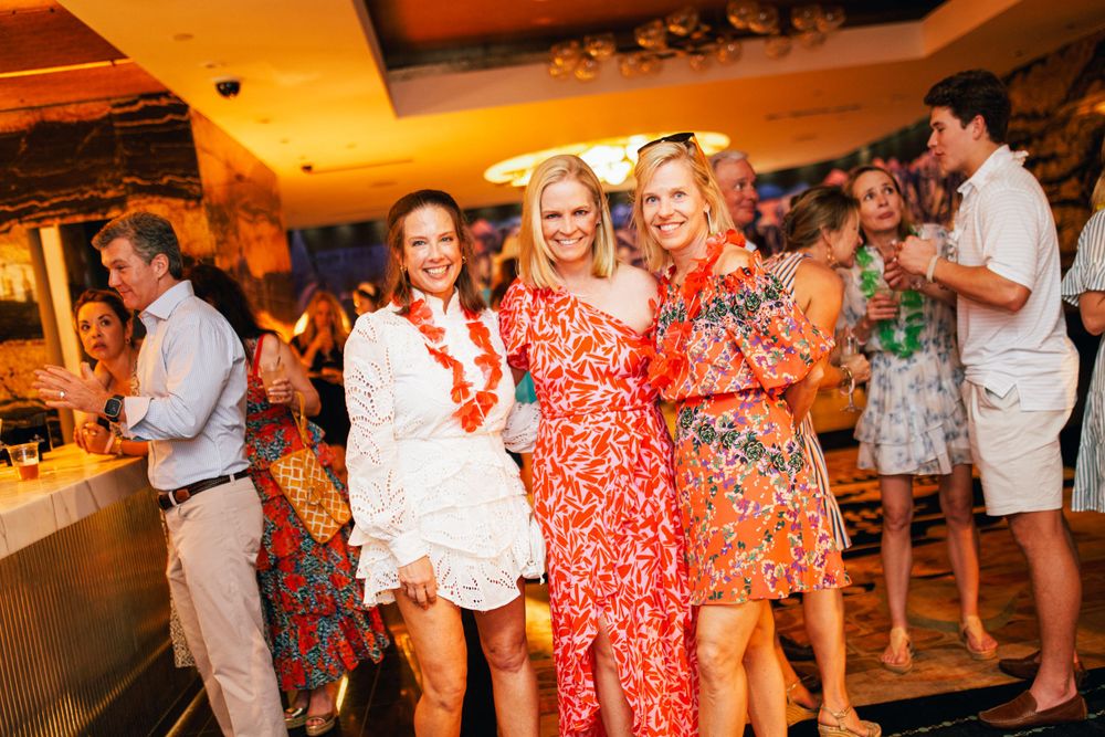Group of friends in colorful floral dresses dancing and celebrating at a lively party.