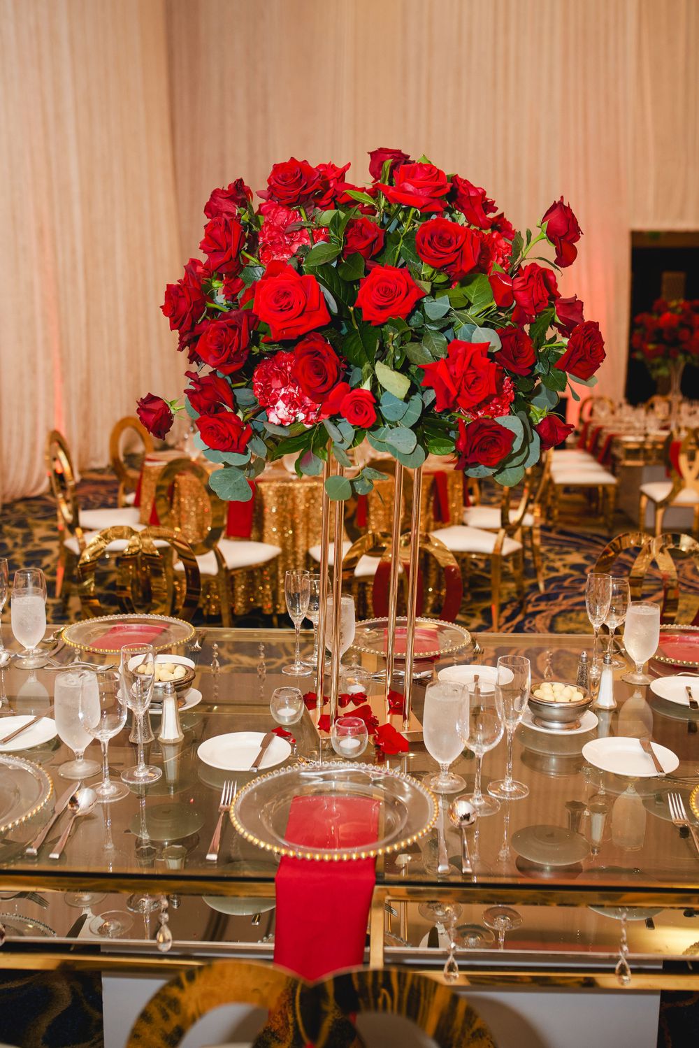 Luxurious table setting featuring tall red rose centerpiece and gold accents.