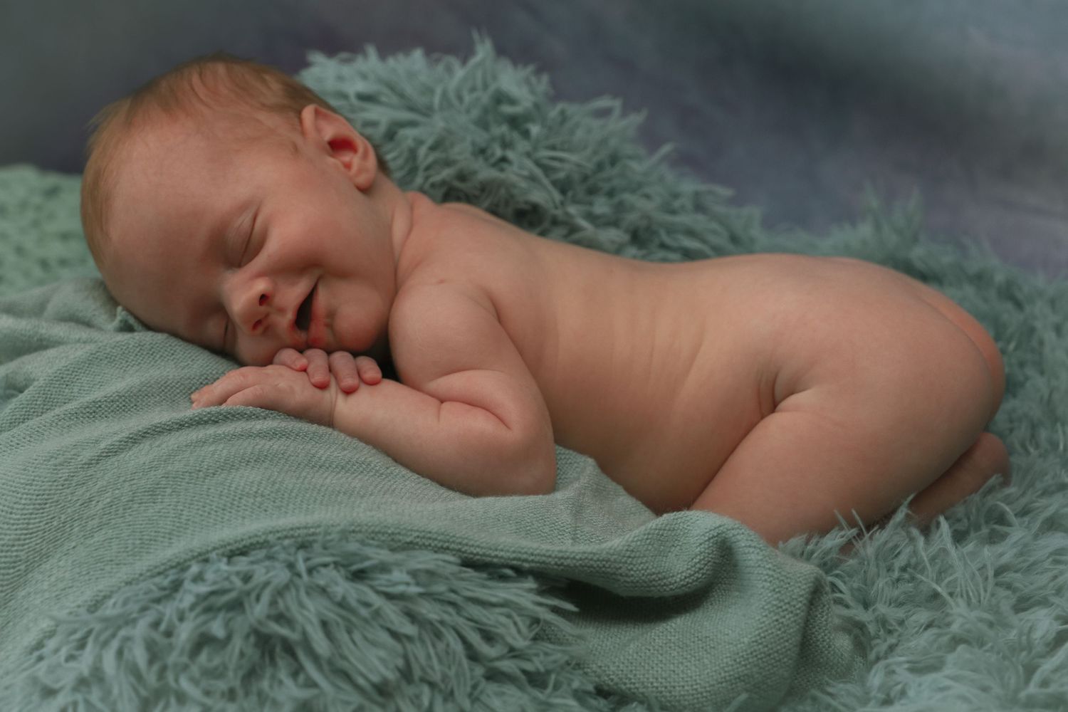 A sleeping baby rests peacefully on soft teal-colored bedding.