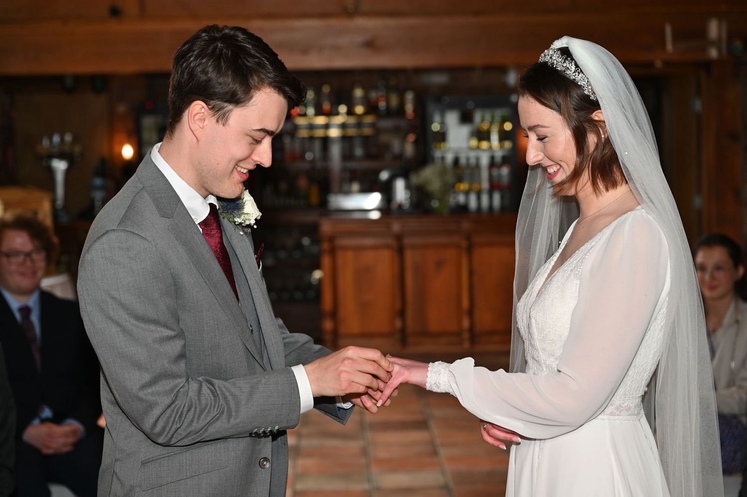 Wedding ceremony moment of ring exchange in wooden interior setting.