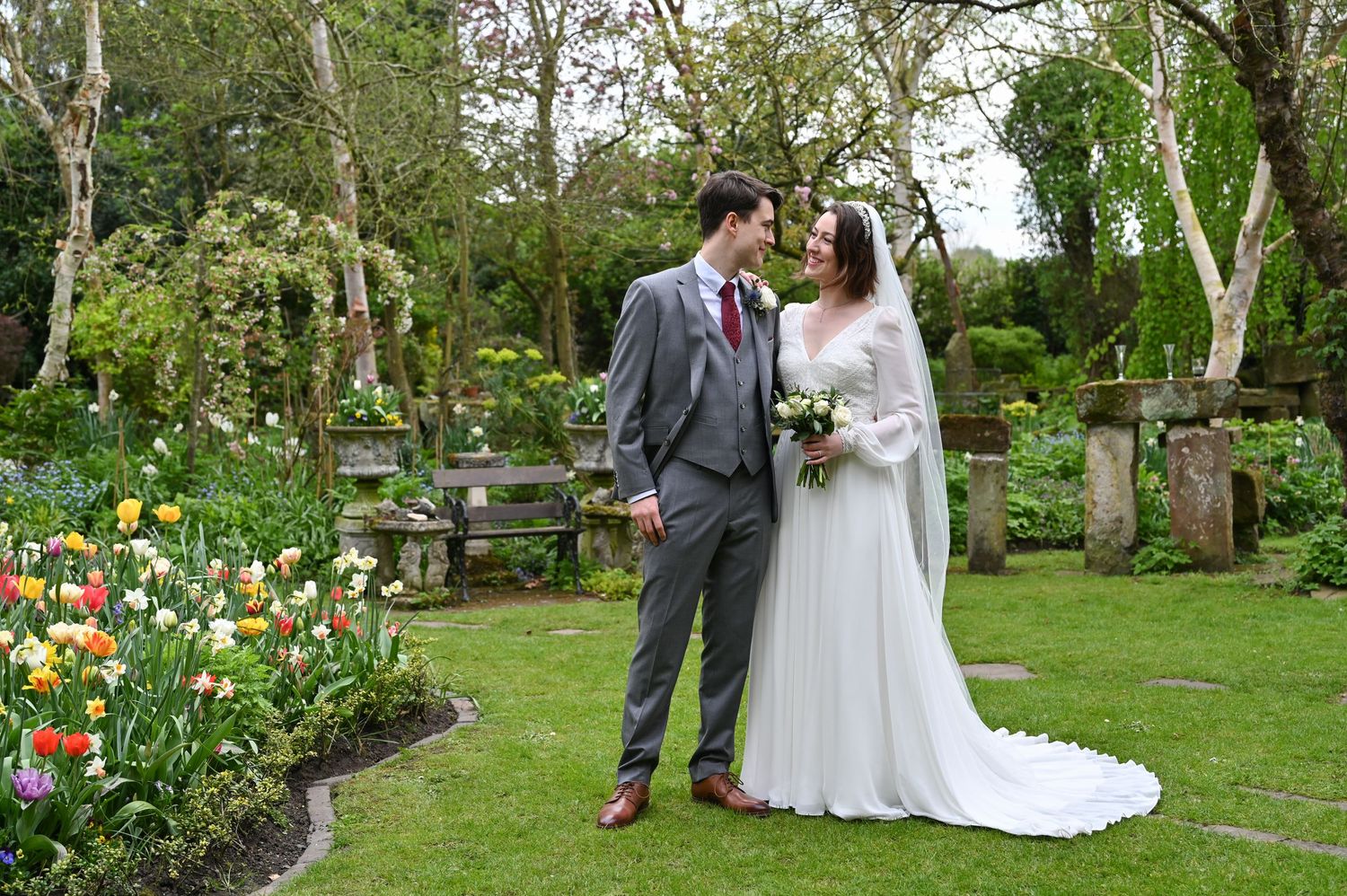 A romantic garden wedding photo with tulips blooming and a classic gray suit against a lush green backdrop.