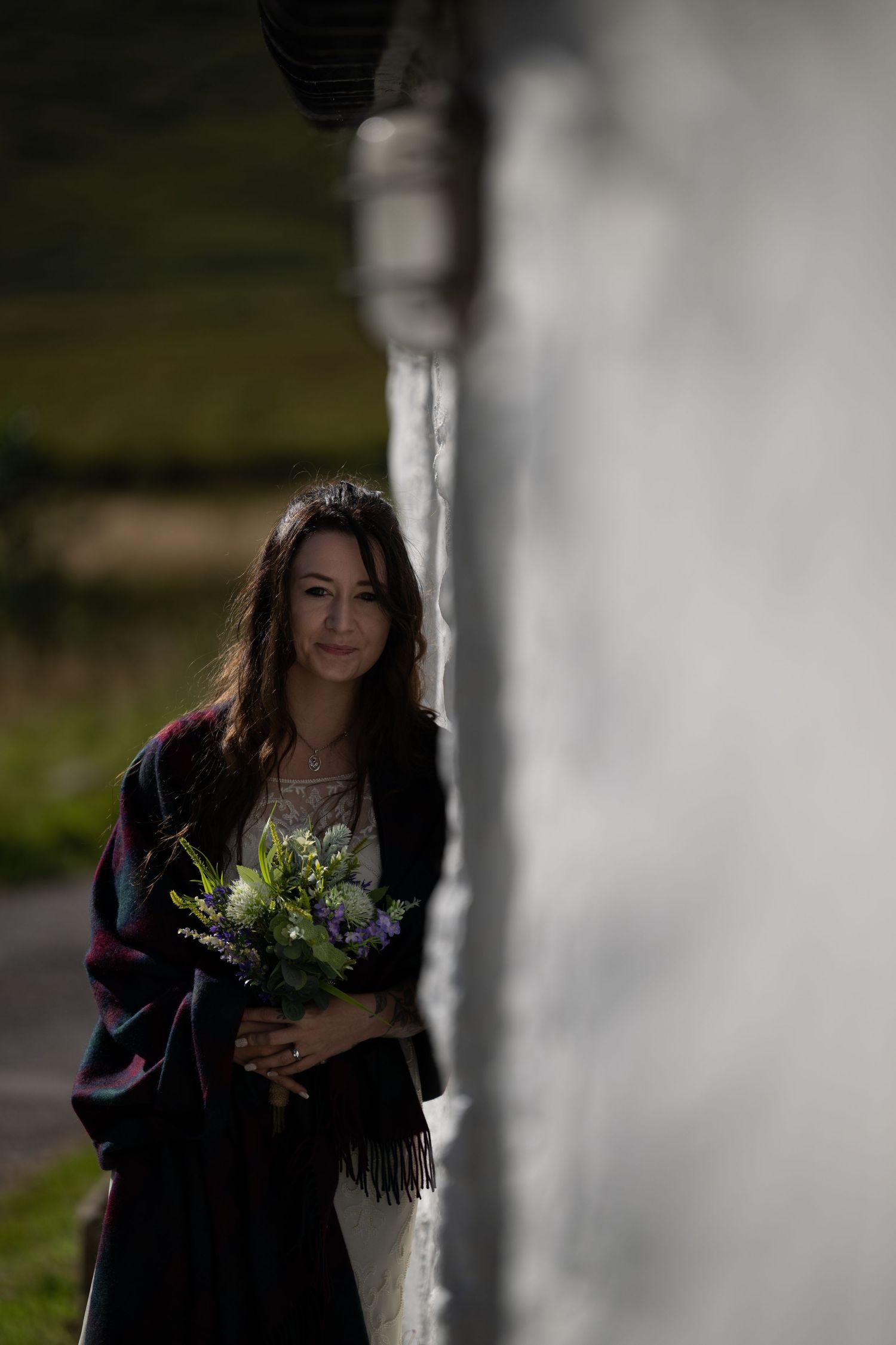 Artistic bridal portrait with natural light streaming through rustic white wall.