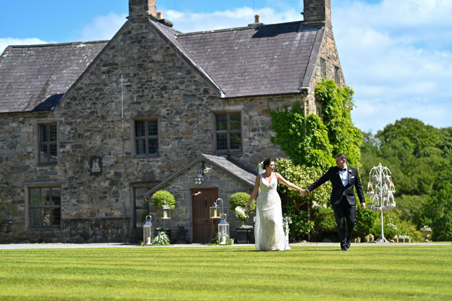Wedding couple poses on lawn in front of a historic stone house with ivy-covered walls.
