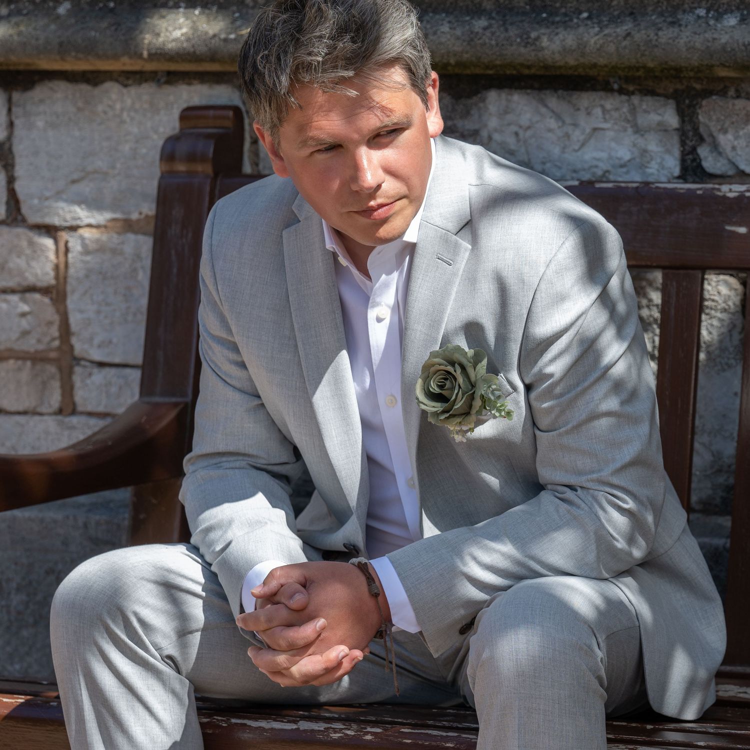 A person in a light gray suit sits thoughtfully on a wooden bench.