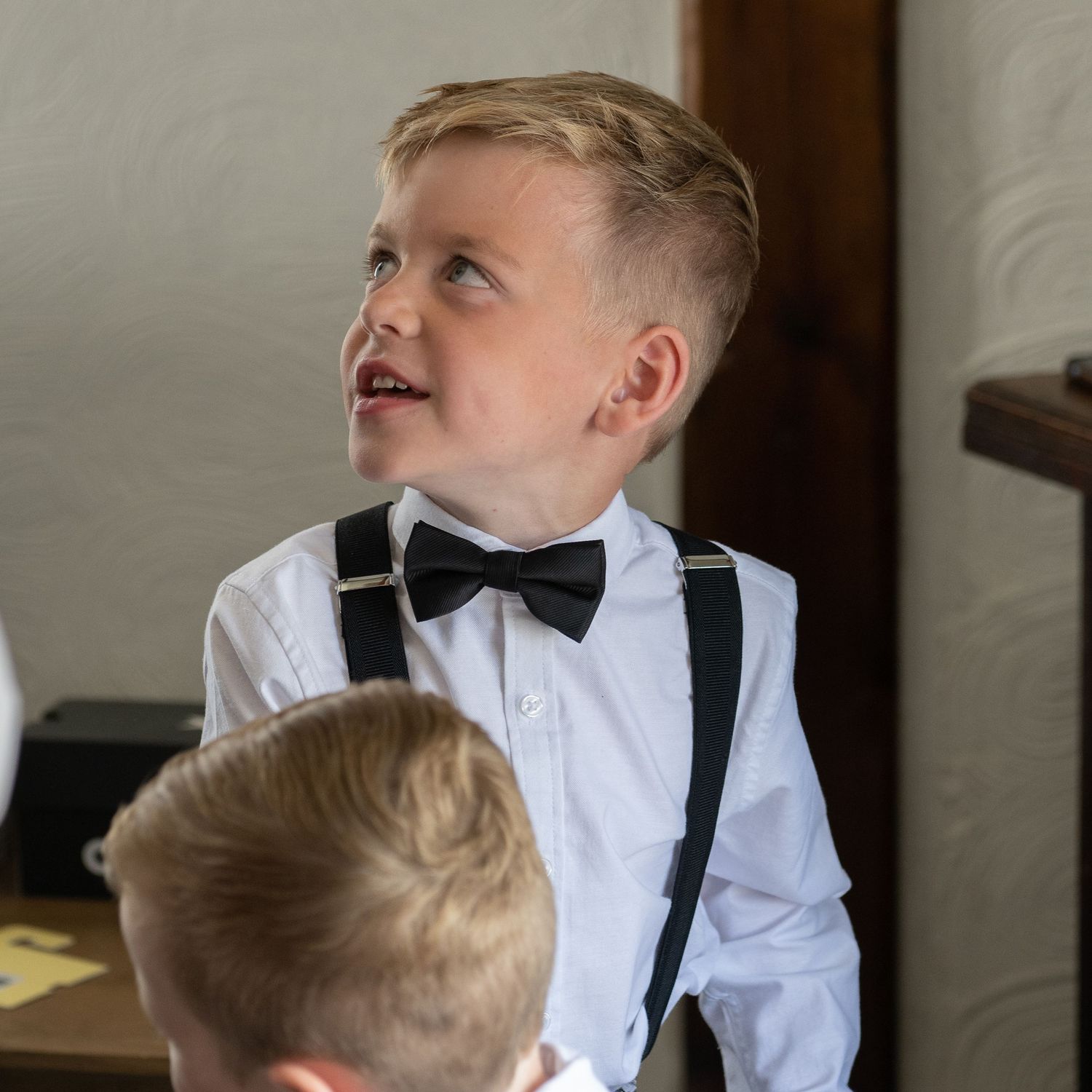 Young ring bearer in bow tie and suspenders looking up with excitement.