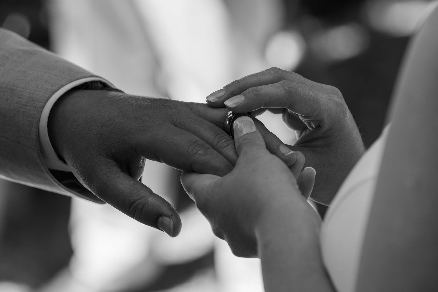 Close-up black and white photo of hands exchanging wedding rings during a ceremony.