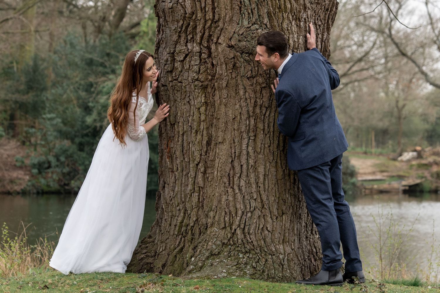 Playful wedding photo with couple on opposite sides of large tree trunk.