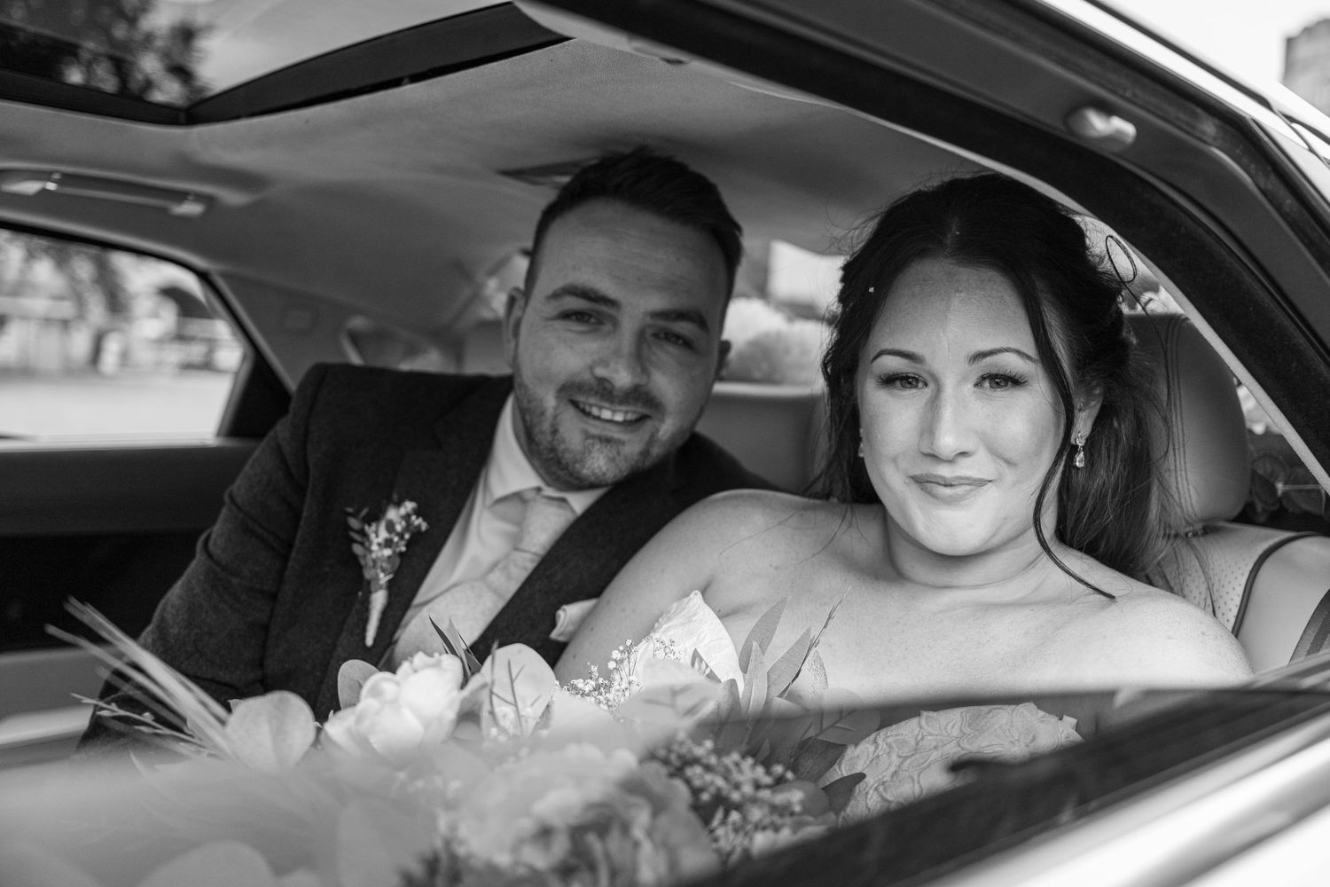 Happy newlyweds sitting in their wedding car.