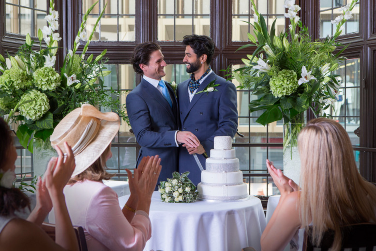 Wedding celebration in an elegant conservatory with hydrangea decorations and a white tiered cake.