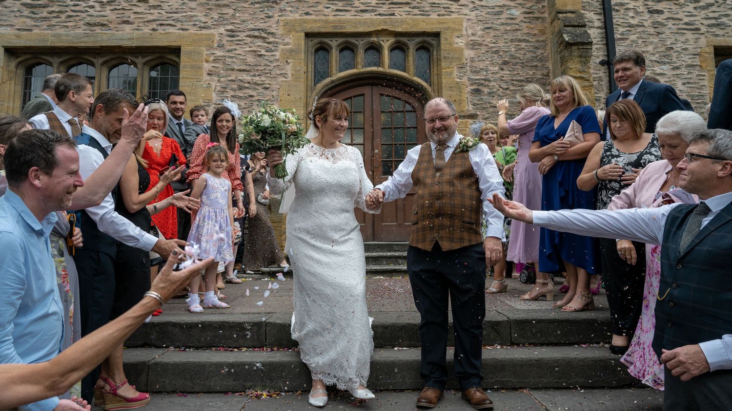 Wedding guests throw confetti at newlyweds on stone church steps.