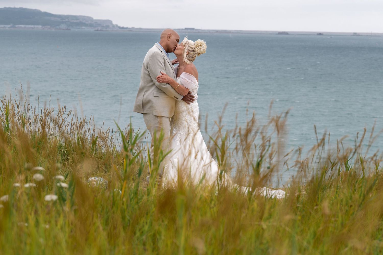 Couple embracing on a coastal clifftop with ocean views in the background.