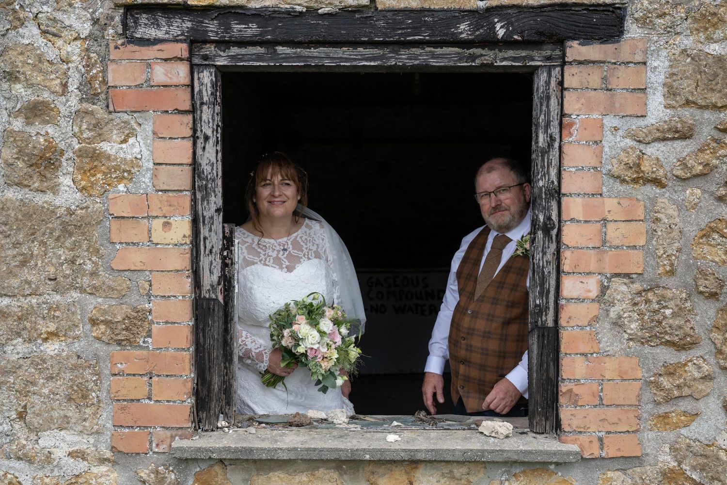 A couple poses in a rustic brick window frame on their wedding day.