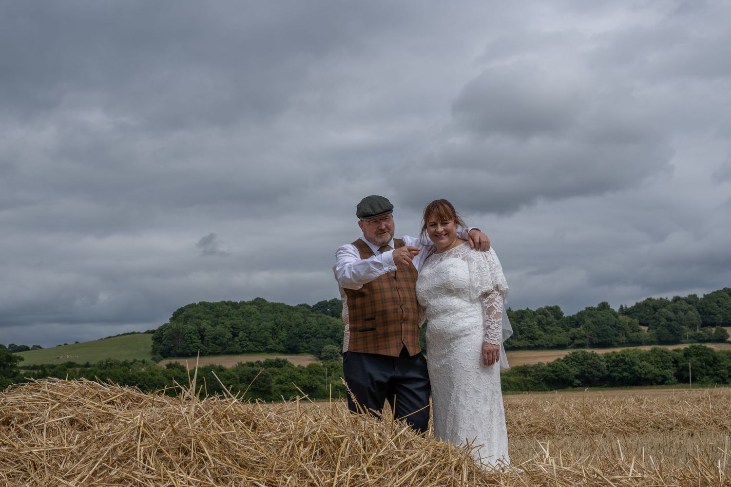 Rustic countryside wedding portrait on hay bales under moody gray skies.