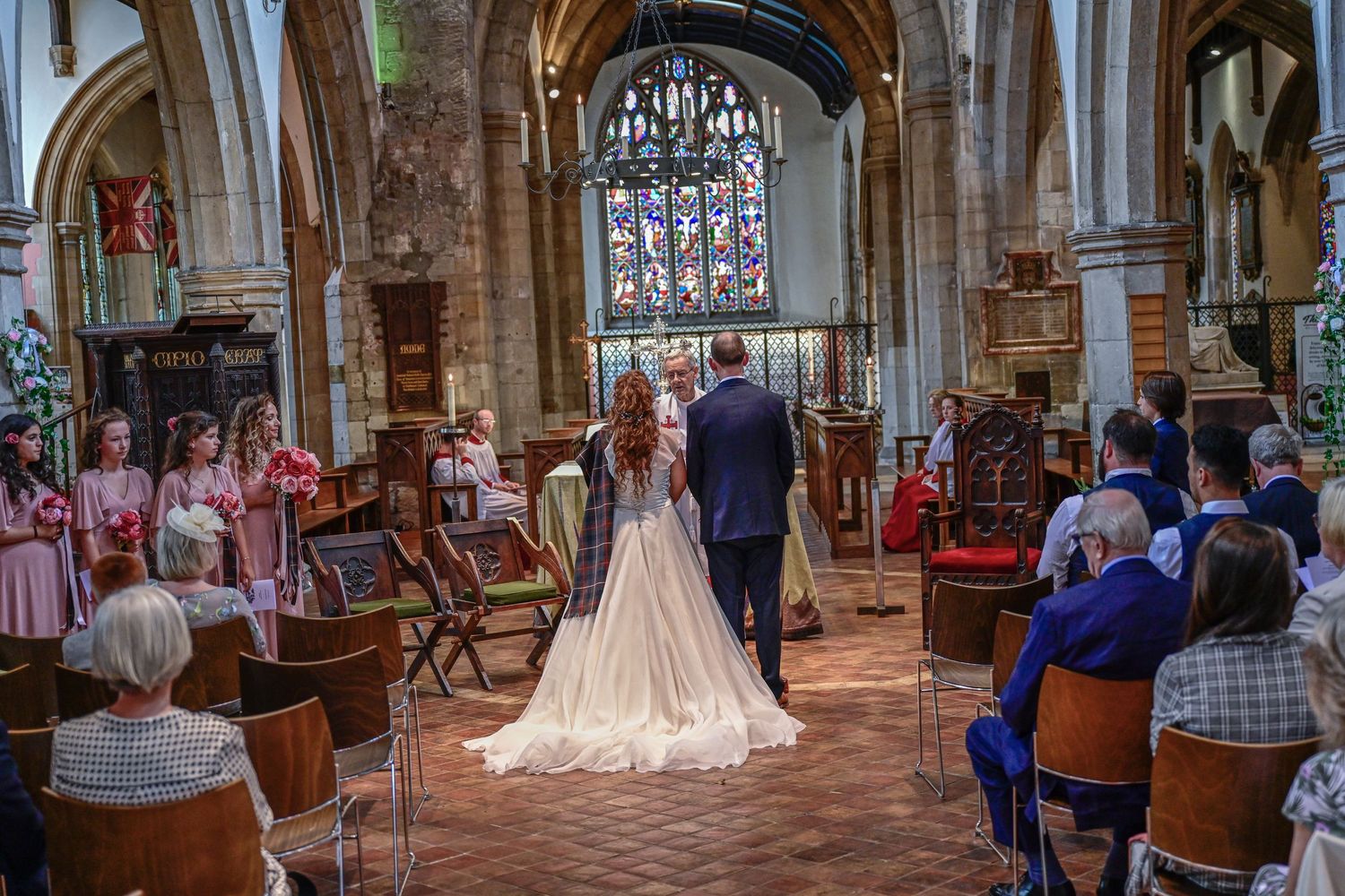 Church wedding ceremony with stained glass windows and guests seated in wooden pews.