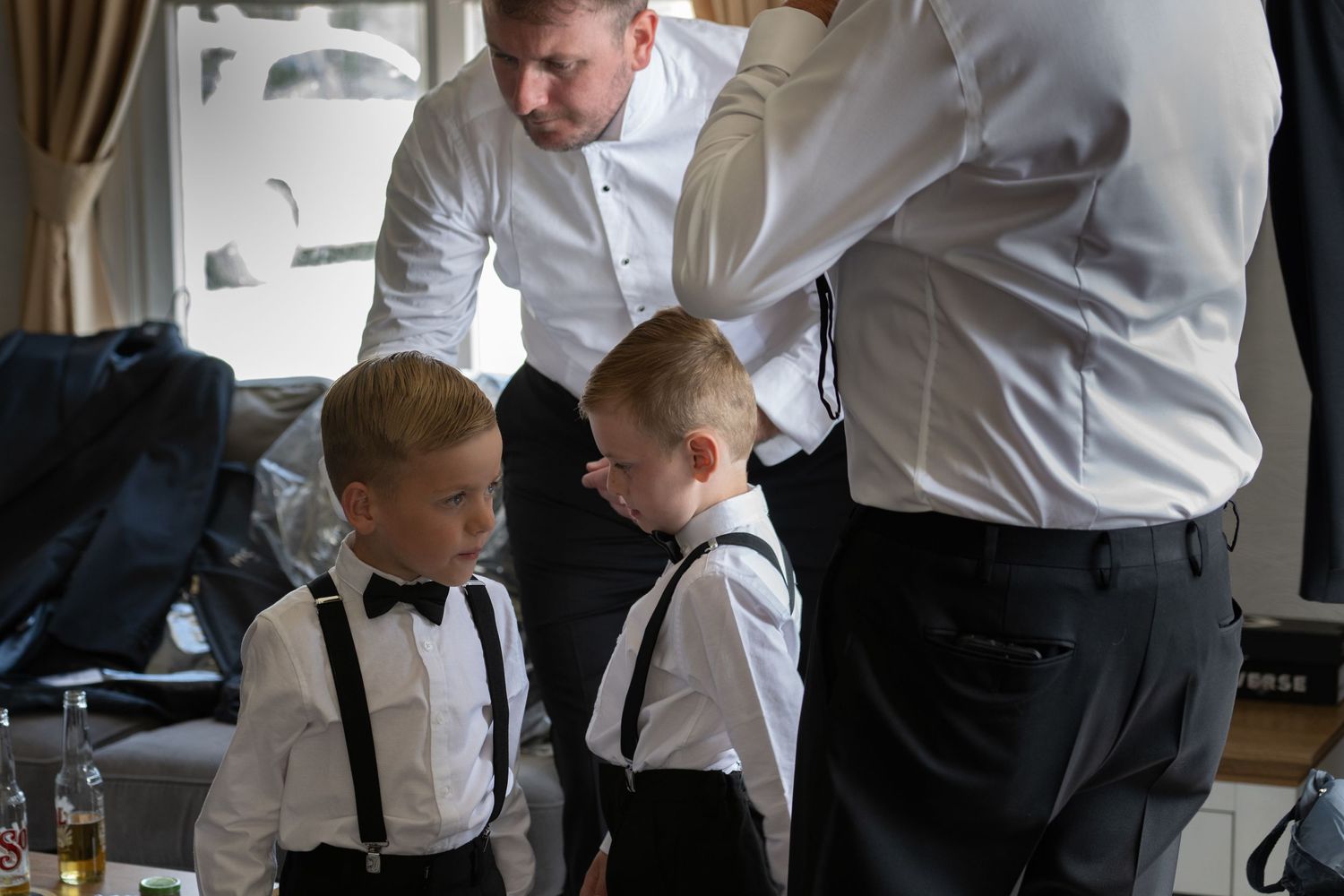 Two young boys in formal wear with bow ties and suspenders getting ready.