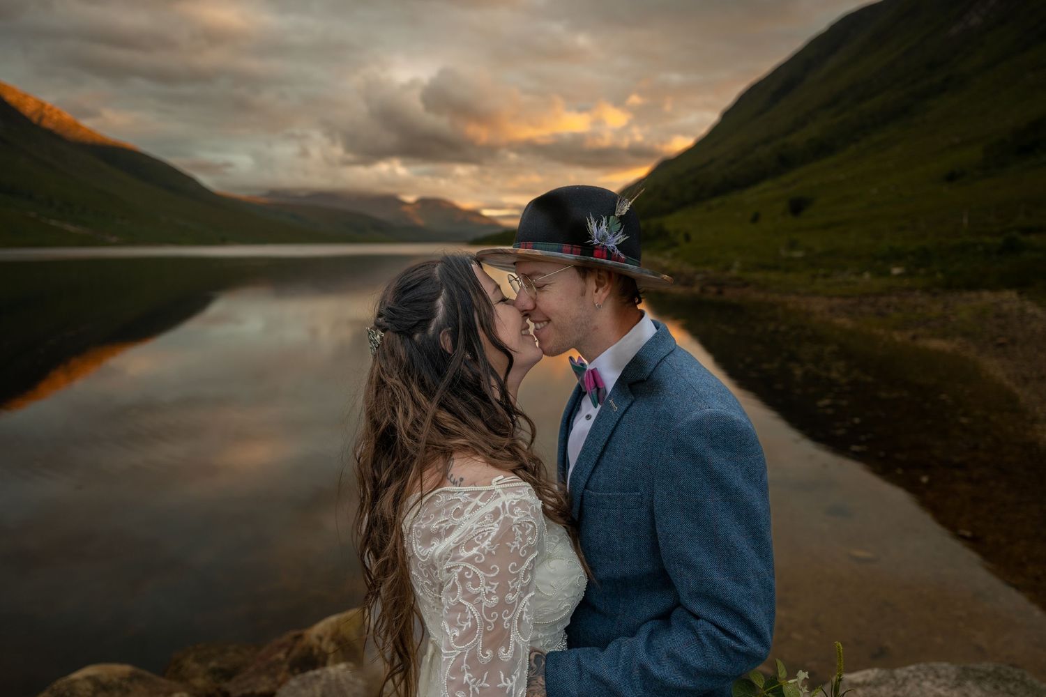 Romantic sunset wedding portrait by scenic mountain lake with dramatic clouds.