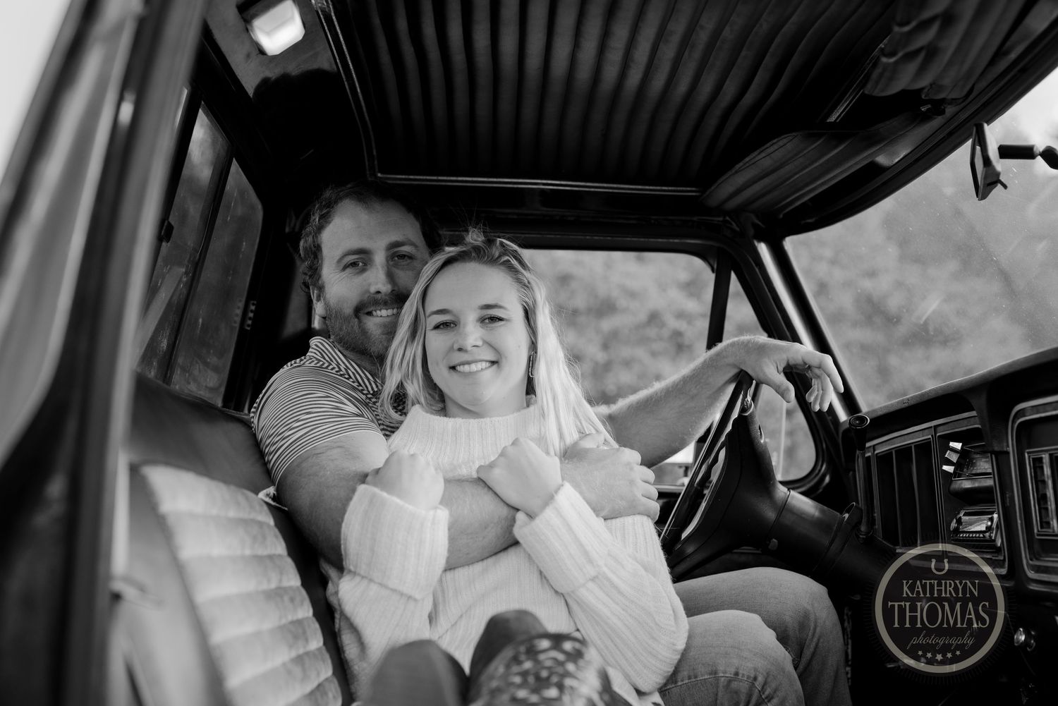 Black and white candid photo of a couple sharing joyful moment inside classic truck cabin.