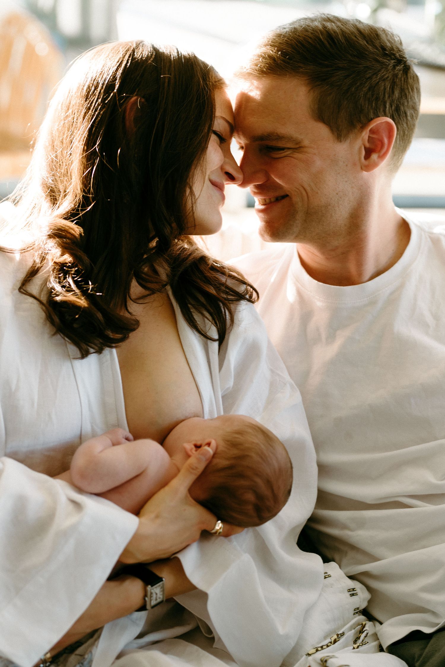 Intimate family moment with newborn baby in soft window light.