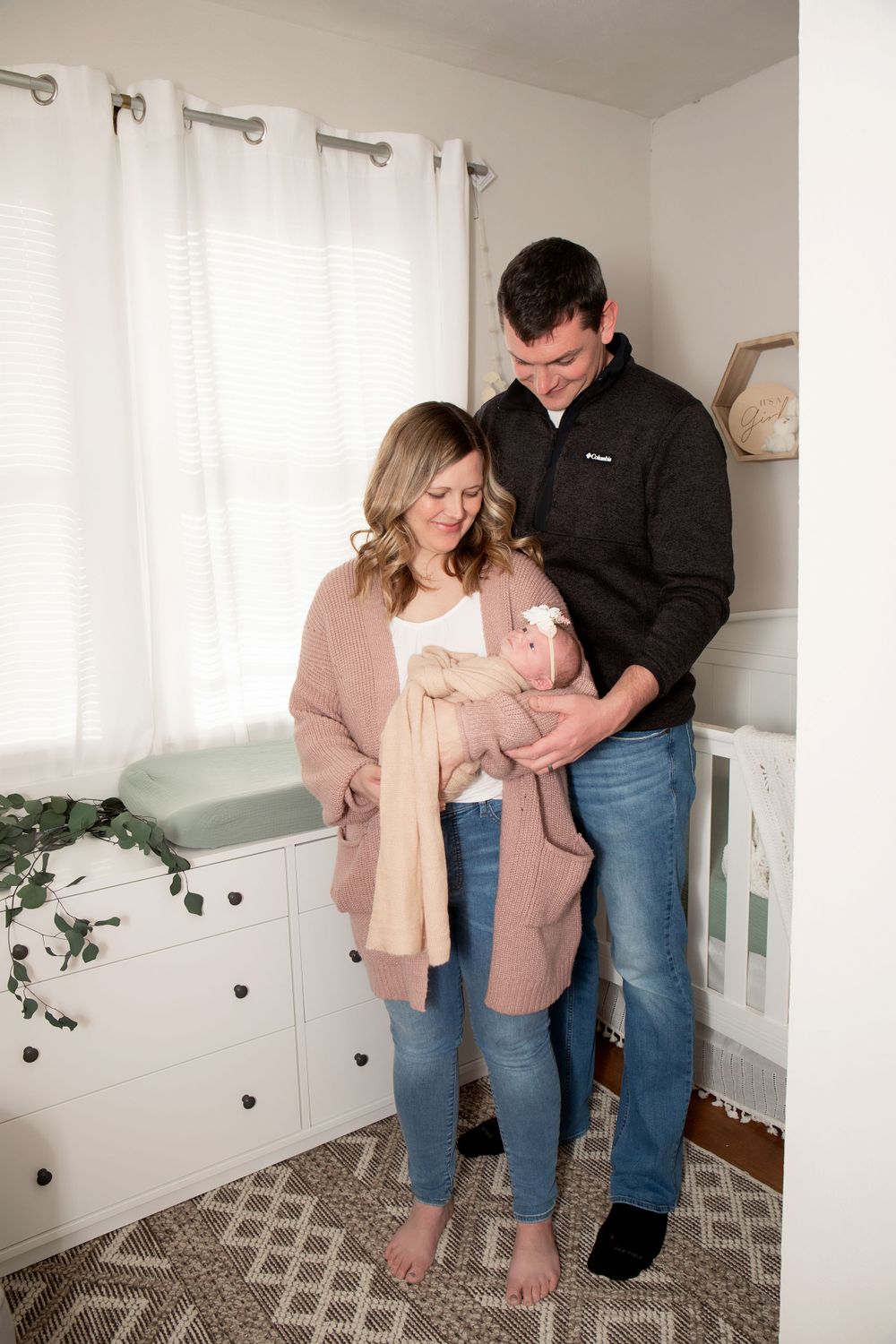 Family sharing an intimate moment together in a bright nursery setting with white curtains.