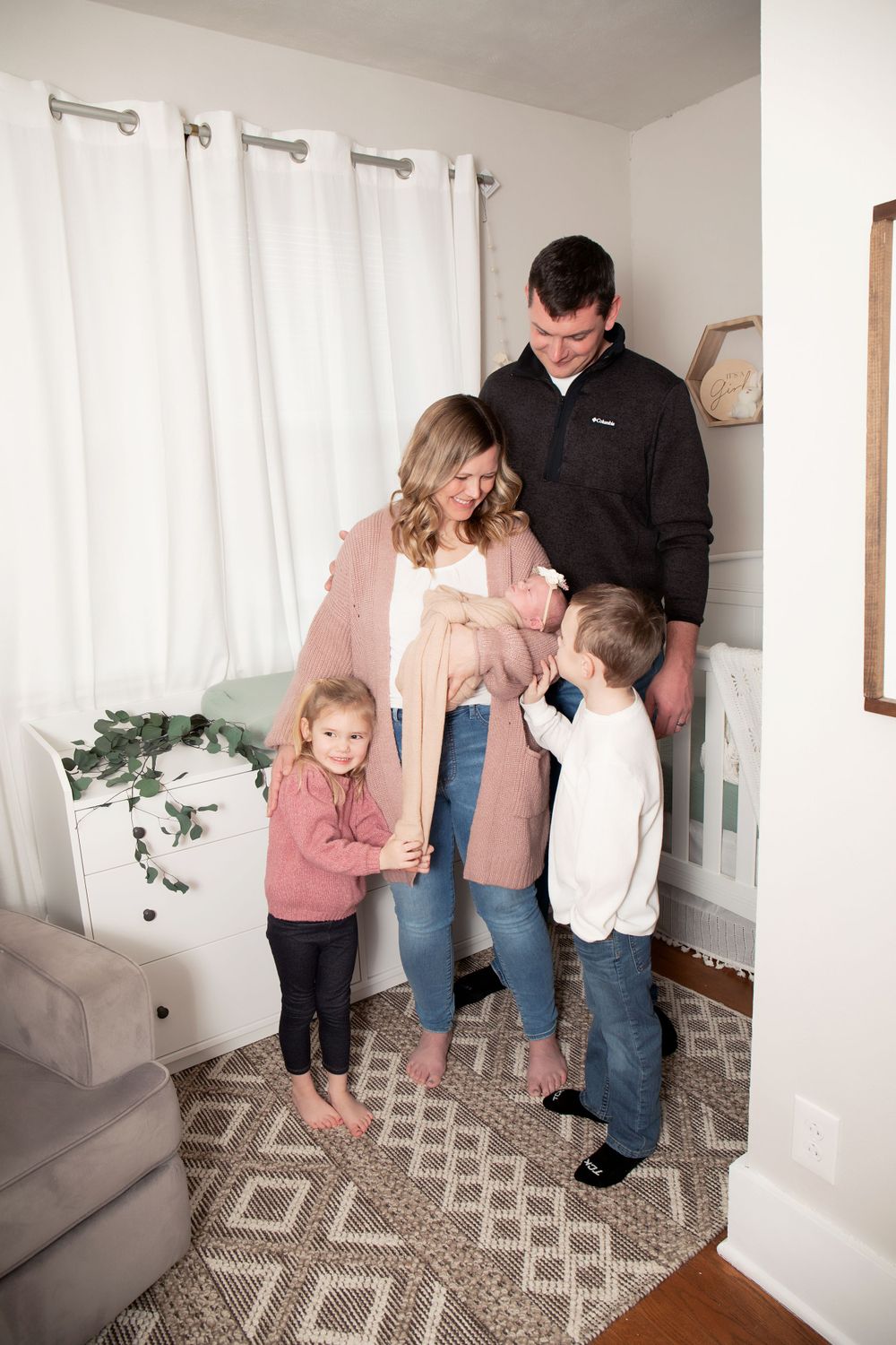 Candid family moment captured in a modern nursery with patterned rug and white curtains.