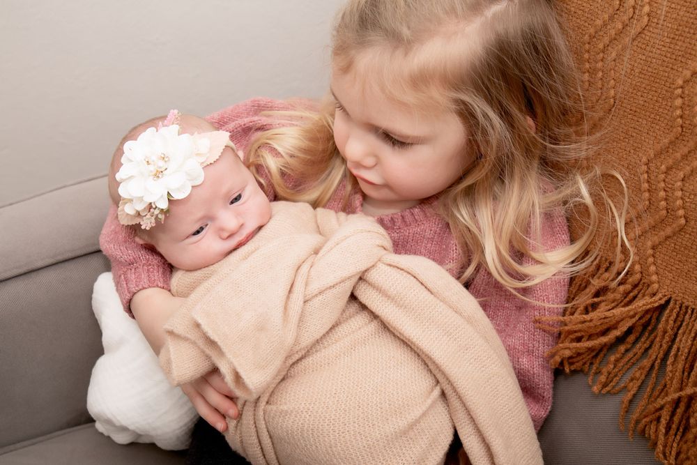 Sweet moment between siblings on a cozy gray sofa with an orange throw blanket.