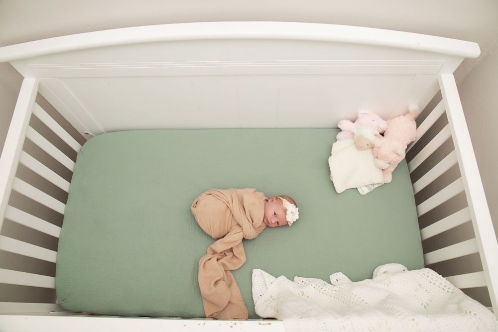 Overhead view of white crib with mint green mattress and baby in beige swaddle.