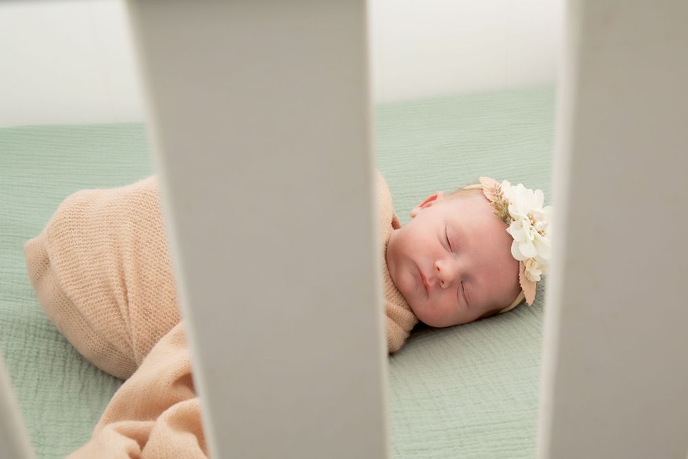 Close-up view through crib slats of sleeping baby on mint green mattress.