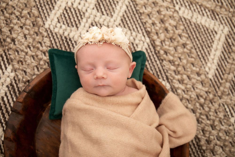 Peaceful sleeping baby with floral crown on dark green pillow against geometric pattern.