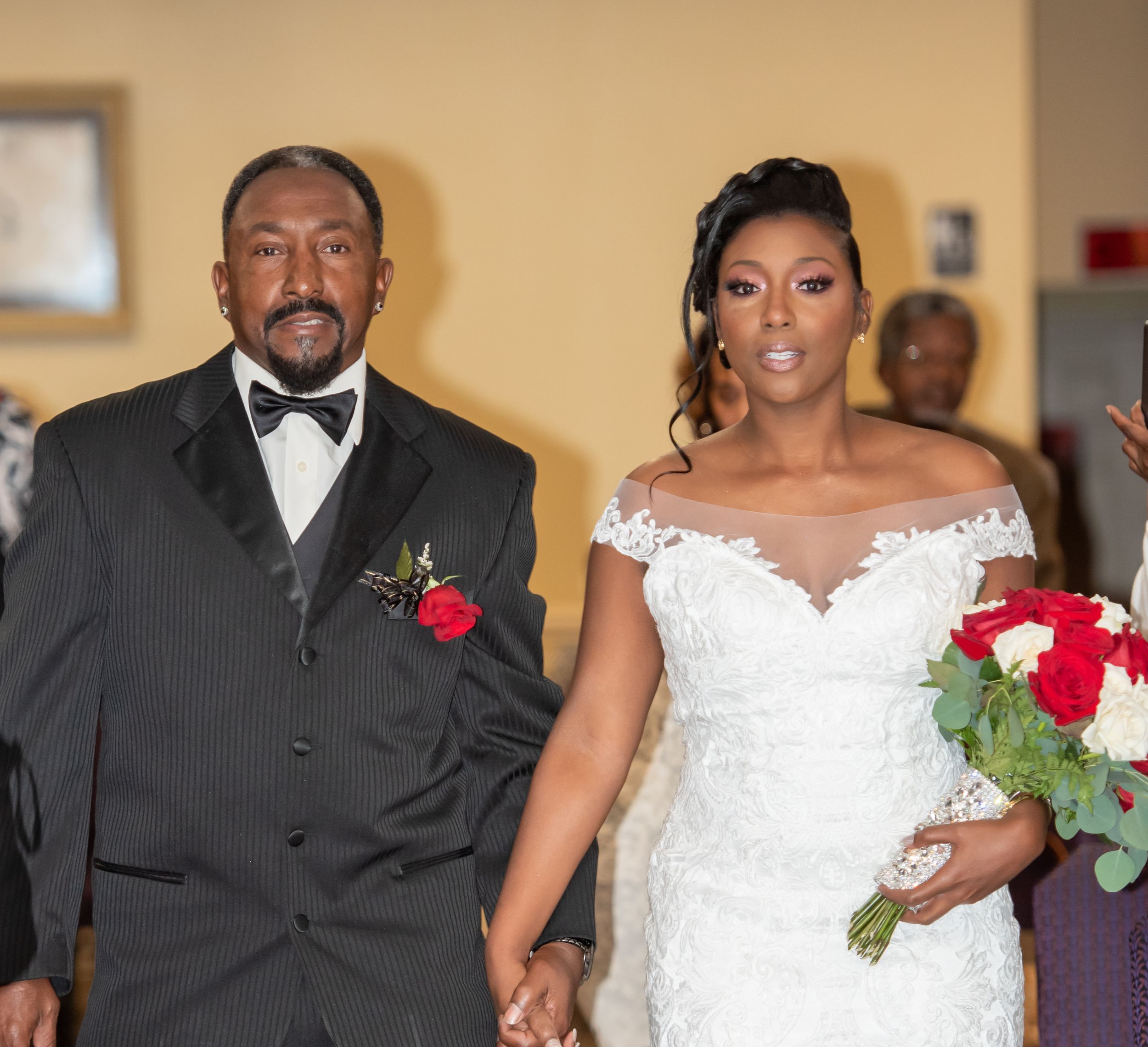 A moment from a wedding ceremony shows a couple walking down the aisle with red rose bouquet accents.