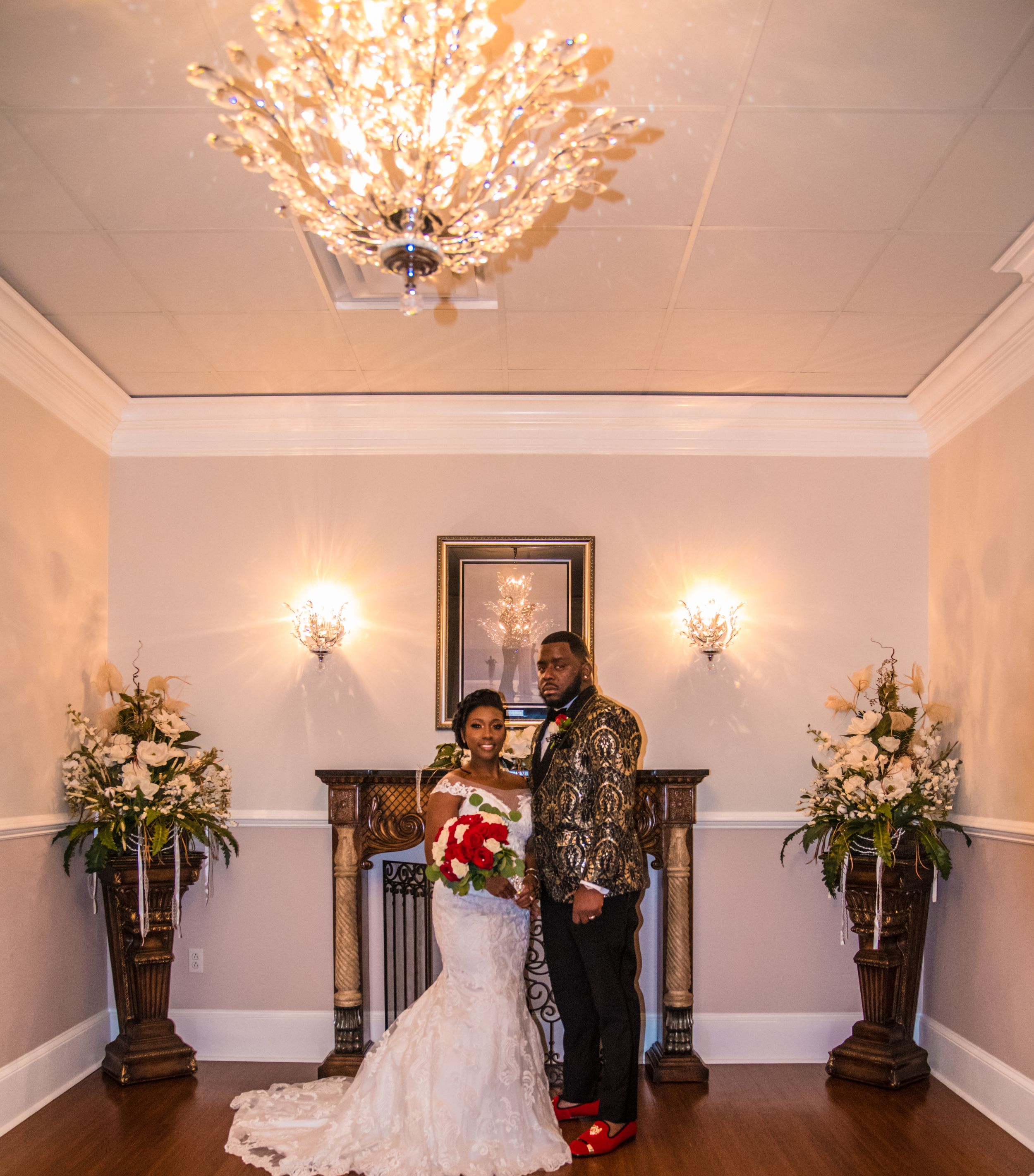 An elegant wedding reception room with crystal chandelier, sconces, and floral arrangements on pedestals.