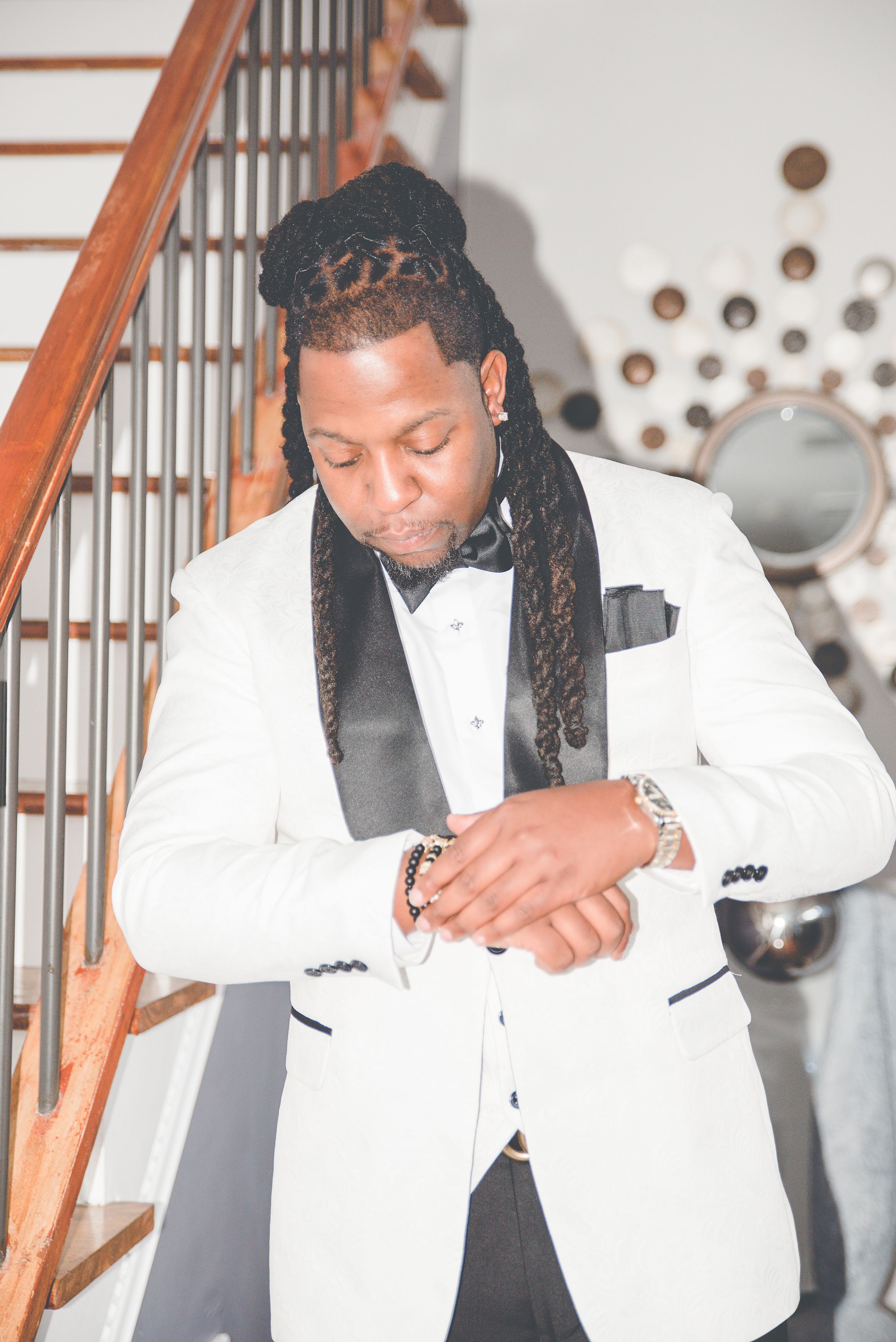 A white tuxedo jacket with black lapels and bowtie is captured near a staircase with decorative wall accents.