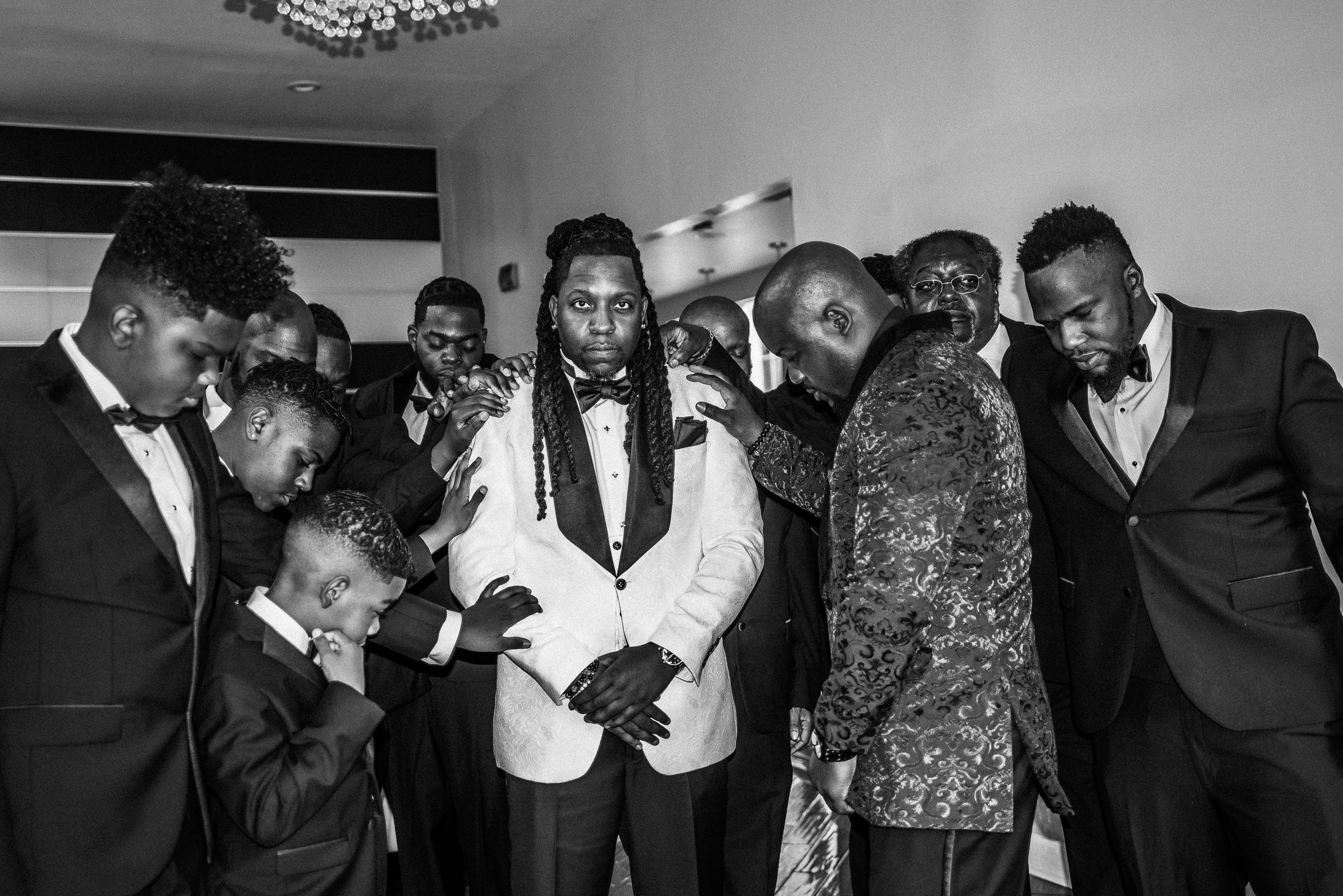 A black and white photo captures a wedding party gathering in formal attire.