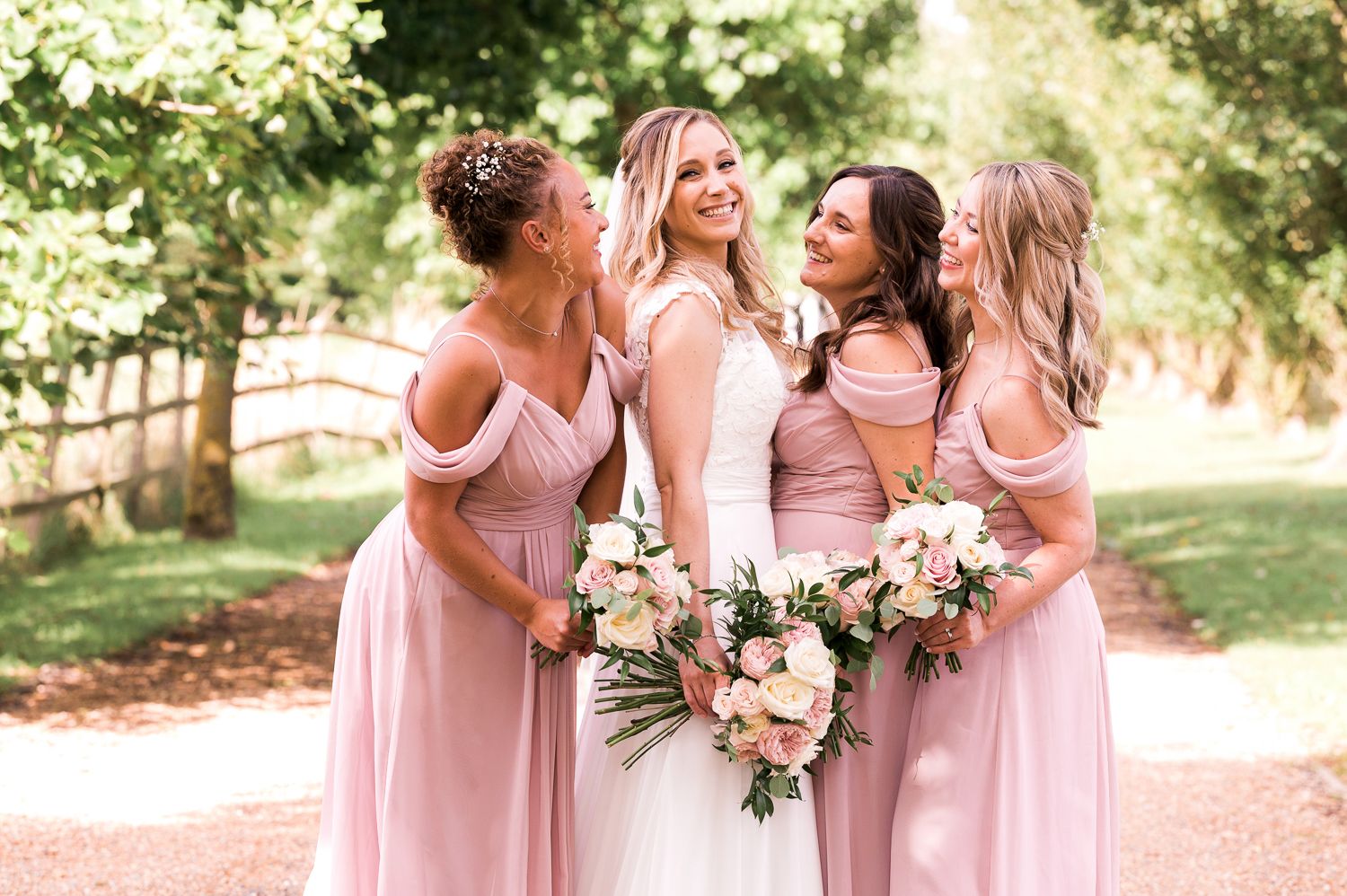 Bride and bridesmaids in pink dresses share joyful moment outdoors.