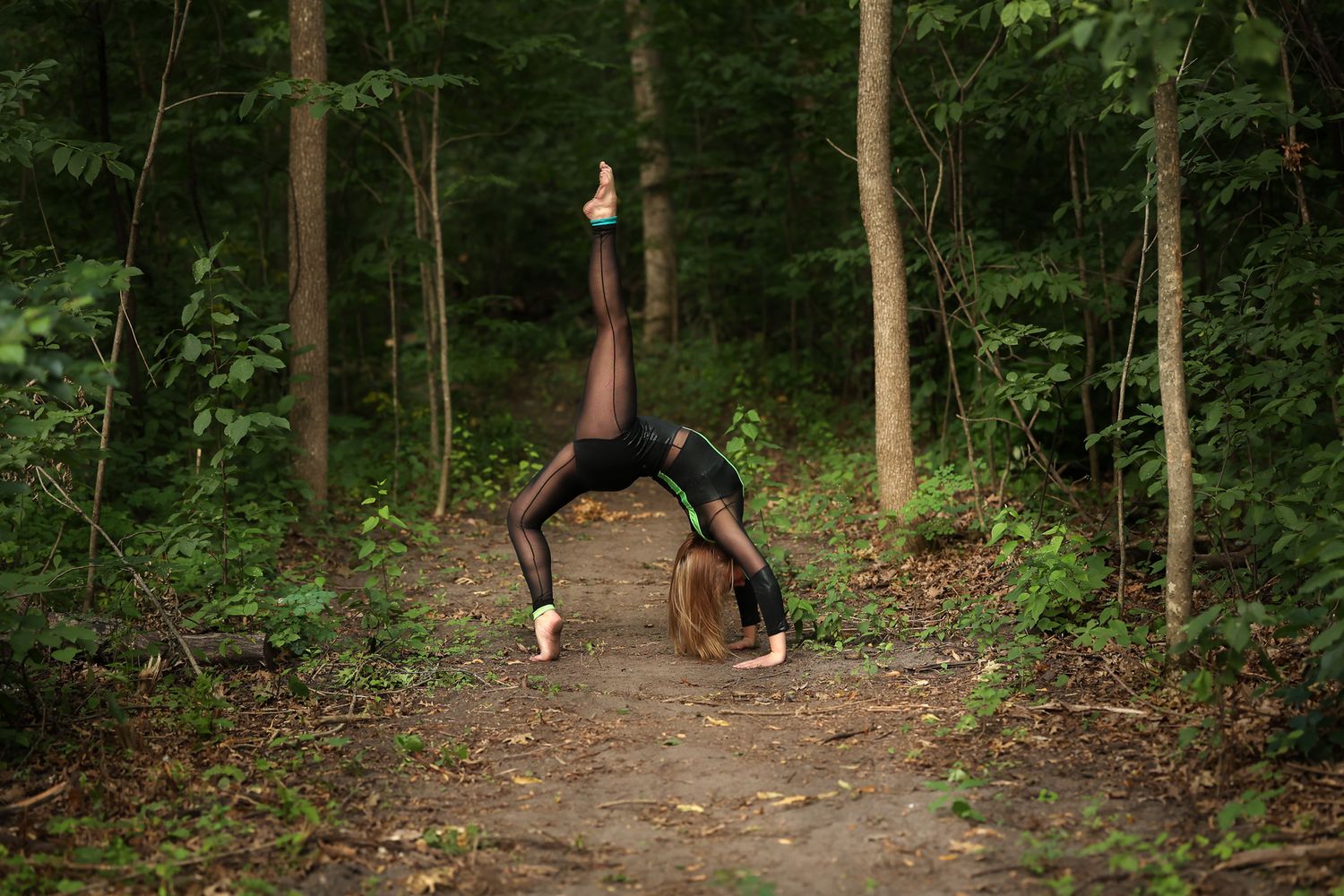 Graceful dancer performing backbend on forest path wearing black leotard.